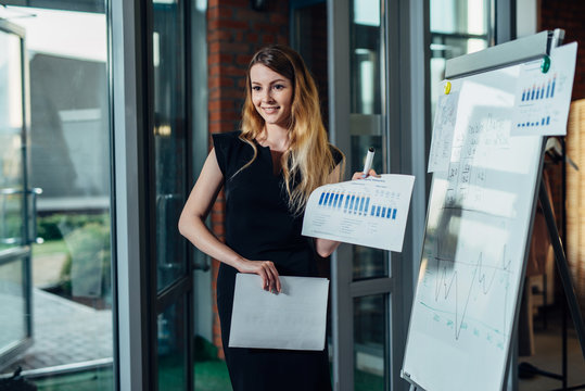Portrait of young female entrepreneur wearing formal dress holding the financial report standing in the office