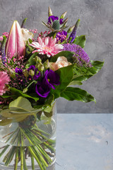 Purple and pink flowers bouquet. Glass vase. Gray backround.