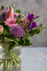 Purple and pink flowers bouquet. Glass vase. Gray backround.