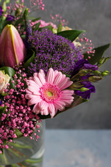 Purple and pink flowers bouquet. Glass vase. Gray backround.