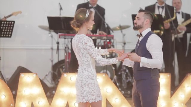 Man and woman dance at party with live music band playing on stage background. Dancers couple in love wear festive outfits suit vest and white lace design dress diamond diadem at charity ball indoors