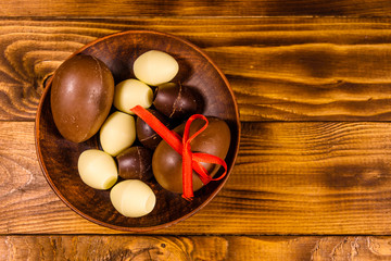 Ceramic plate with chocolate easter eggs on wooden table. Top view