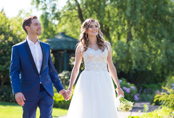 bride and groom smiling each other walking in the park for hands