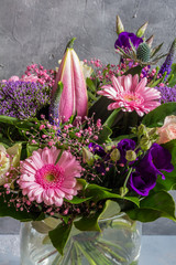 Purple and pink flowers bouquet. Glass vase. Gray backround.