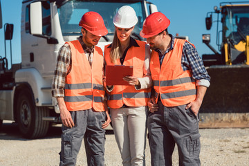truck drivers and dispatcher in front of lorries in freight forwarding company looking at tablet...