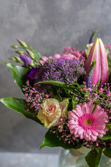 Purple and pink flowers bouquet. Glass vase. Gray backround.