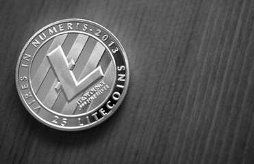 Black and white photo of silver litecoin on wooden background, close up