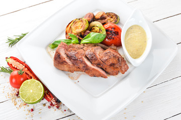 Pork steak with grilled vegetables on a plate. On a wooden background. Top view. Copy space.