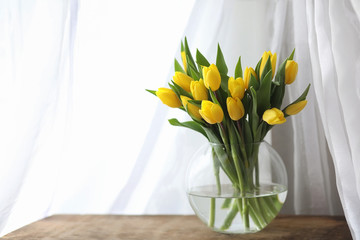 A bouquet of yellow tulips in a vase on the windowsill. A gift t