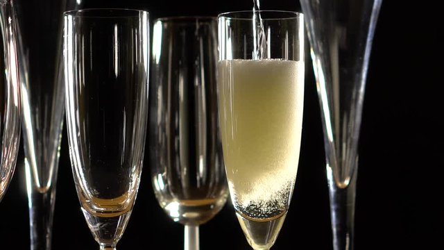Closeup of champagne pouring into a champagne glass against a black background.