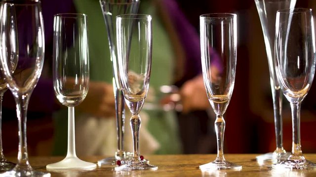With a group of various champagne glasses in the foreground, someone in the background cleans the glasses and sets them into place.