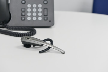 Wireless headset is on the white table with black IP or office phone at behind