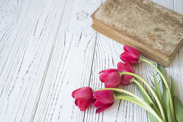 old book and tulips on white wooden table