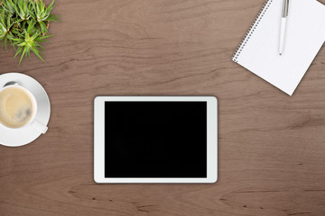 Brown wooden office desk top view with tablet pc, notepad, pen, plant and cup of coffee