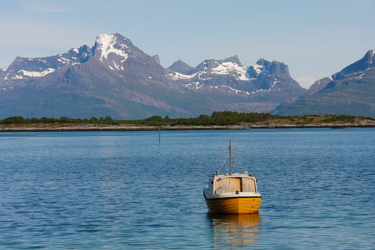 Old small fihing boat floating on calm water of norwegian fjord.