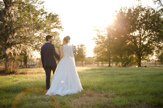 Hispanic Bride And Groom Portrait On Wedding Day Walking In A Field