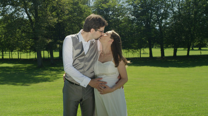 Fototapeta premium Excited parents to be share a tender kiss in the sunlit park after their wedding