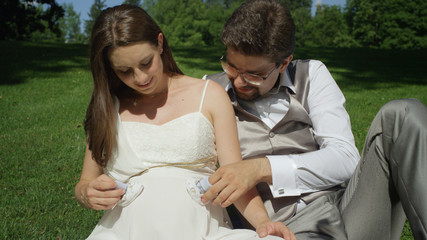 CLOSE UP: Young couple gently pressing tiny baby socks on her pregnant belly