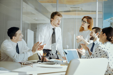 Unexpected news. Pleasant young man looking utterly shocked and jaw-slacked while being surrounded by his colleagues telling him surprising news