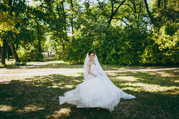 Beautiful wedding photosession. The smiling bride in a white lace dress with a plume, long sleeves,...