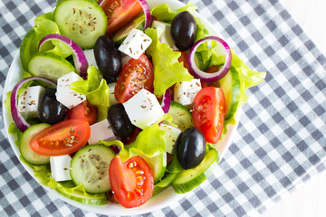 Fresh Greek salad made of cherry tomato, ruccola, arugula, feta, olives, cucumbers, onion and spices. Caesar salad in a white bowl on wooden background. Healthy organic diet food concept.