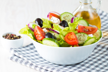 Fresh Greek salad made of cherry tomato, ruccola, arugula, feta, olives, cucumbers, onion and spices. Caesar salad in a white bowl on wooden background. Healthy organic diet food concept.