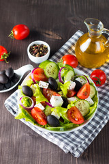 Fototapeta na wymiar Fresh Greek salad made of cherry tomato, ruccola, arugula, feta, olives, cucumbers, onion and spices. Caesar salad in a white bowl on wooden background. Healthy organic diet food concept.