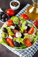 Fresh Greek salad made of cherry tomato, ruccola, arugula, feta, olives, cucumbers, onion and spices. Caesar salad in a white bowl on wooden background. Healthy organic diet food concept.