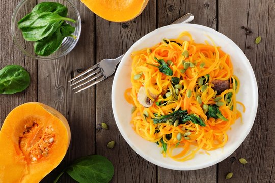Butternut squash spirilized noodles with spinach and pumpkin seeds on dark wood background, Healthy eating concept. Top view, table scene.