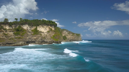 Panoramic view of the endless blue ocean waves crashing into majestic cliff.