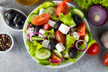 Fresh Greek salad made of cherry tomato, ruccola, arugula, feta, olives, cucumbers, onion and spices. Caesar salad in a white bowl on wooden background. Healthy organic diet food concept.