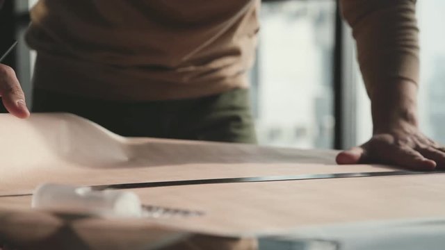 Architect's desk: drawings, tape measure, ruler and other drawing tools. Engineer works with drawings in a bright office, close-up. Insturments and office for designer. Male hands draw with a pencil.