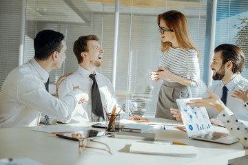 Funny jokes. Adorable young female team leader conducting a meeting with her colleagues and...