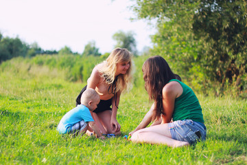 Fototapeta premium Two mothers are playing with children in the green lawn. Happy fun summer photo. Smiling laughing boys with his mom. Sunny day outdoors in nature.