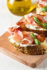Italian tomato, prosciutto, jamon, ham and cheese bruschetta. Tapas, antipasti with chopped vegetables, herbs and oil on grilled ciabatta and baguette bread.