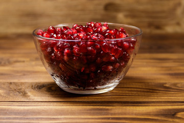 Pomegranate seeds in glass bowl on wooden table