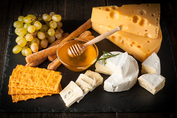 Slate board with various cheese and a glass of red rose wine. Brie. Camembert. Gouda, Masdaam, Roquefort, Cheddar and grapes on a wood with nuts, honey, crackers, blue cheese. Italian, French cheese.