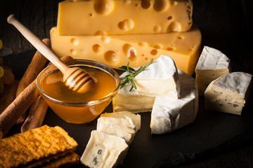 Slate board with various cheese and a glass of red rose wine. Brie. Camembert. Gouda, Masdaam, Roquefort, Cheddar and grapes on a wood with nuts, honey, crackers, blue cheese. Italian, French cheese.