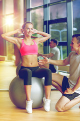 Fototapeta premium smiling man and woman with exercise ball in gym