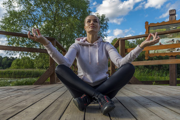 красивая девушка сидит в позе лотоса из йоги на деревянных досках в парке на открытом воздухе 