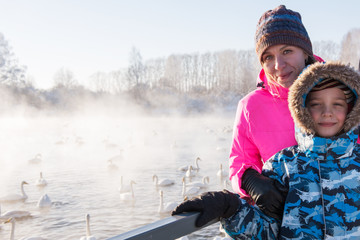 Fototapeta na wymiar Woman at winter nonfreezing lake with white whooping swans. The place of wintering of swans, Altay, Siberia, Russia.