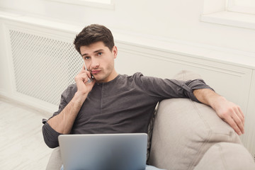 Serious young man at home with laptop and mobile