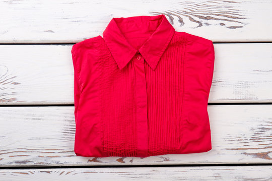 Red folded shirt. Bright wooden desks surface background.