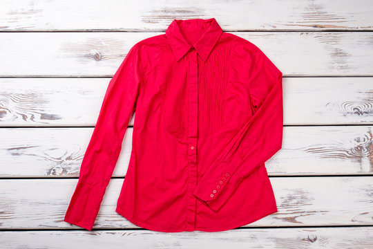 Red women long-sleeve blouse. Bright wooden desks surface background.
