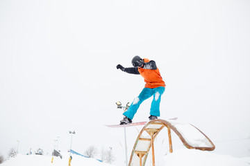 Photo of young sportive man skiing on snowboard with springboard against snowy sky in winter