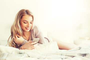 Naklejka premium happy young woman with smartphone in bed at home