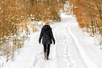 Woman on snow road in winter, girl in black coat, back view in the forest