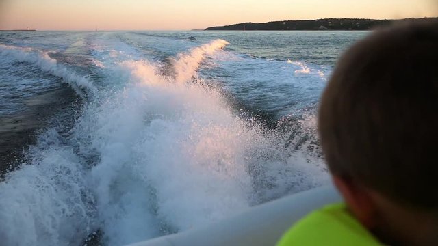 Slow motion of a wake of large boat at sunset on the water and boy