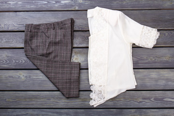Flat lay checkered trousers and lace blouse. White shirt and black pants. Grey wooden desk surface...
