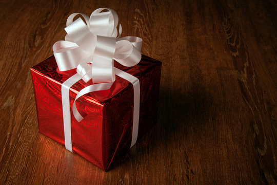 One red festive gift box with a white bow on a wooden table